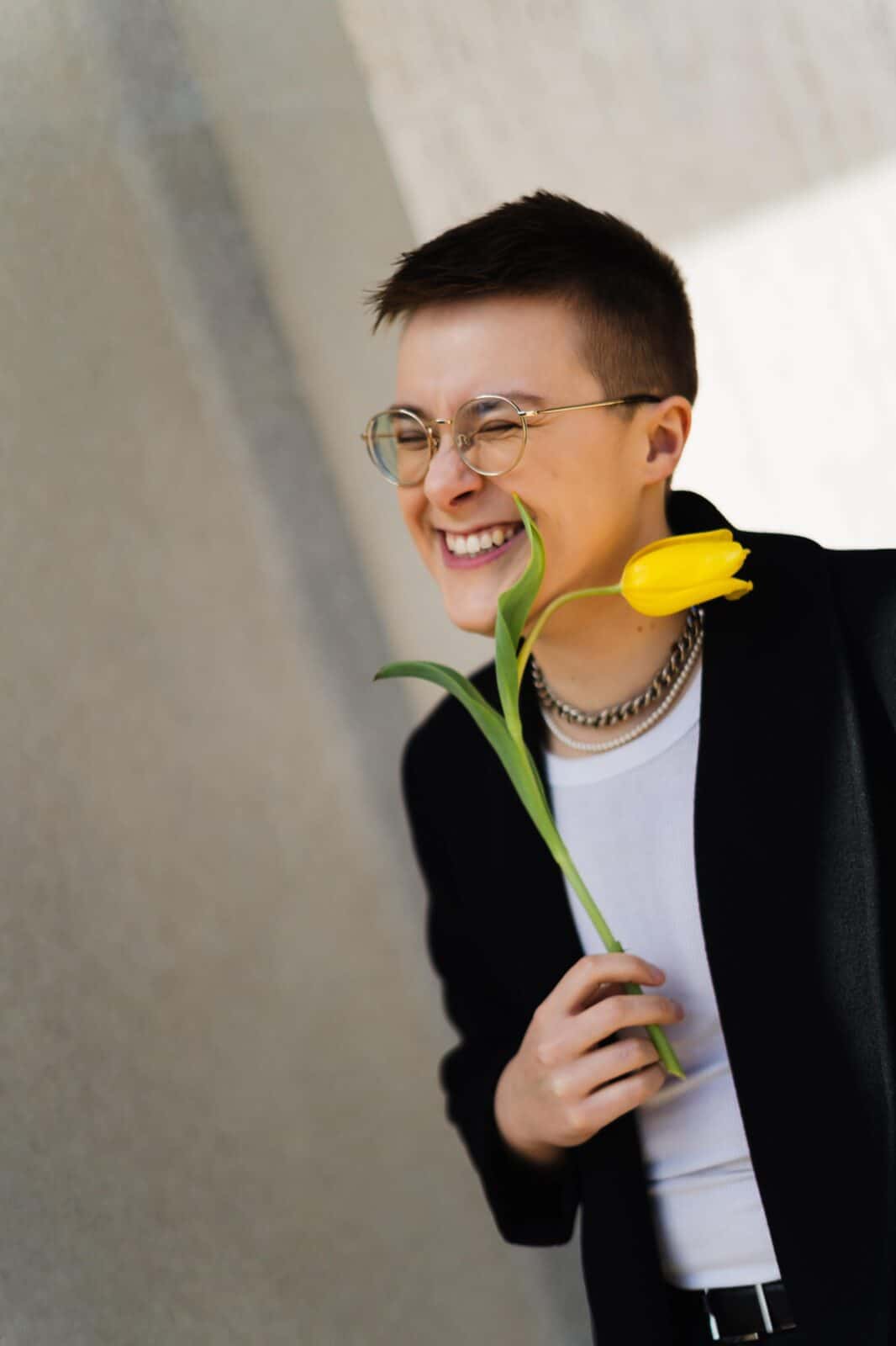 Fiction and creative nonfiction writer, essayist, creator of community and teacher Stevie Billow holds a tulip, laughing, in a t-shirt and blazer. Press photo courtesy of the artist