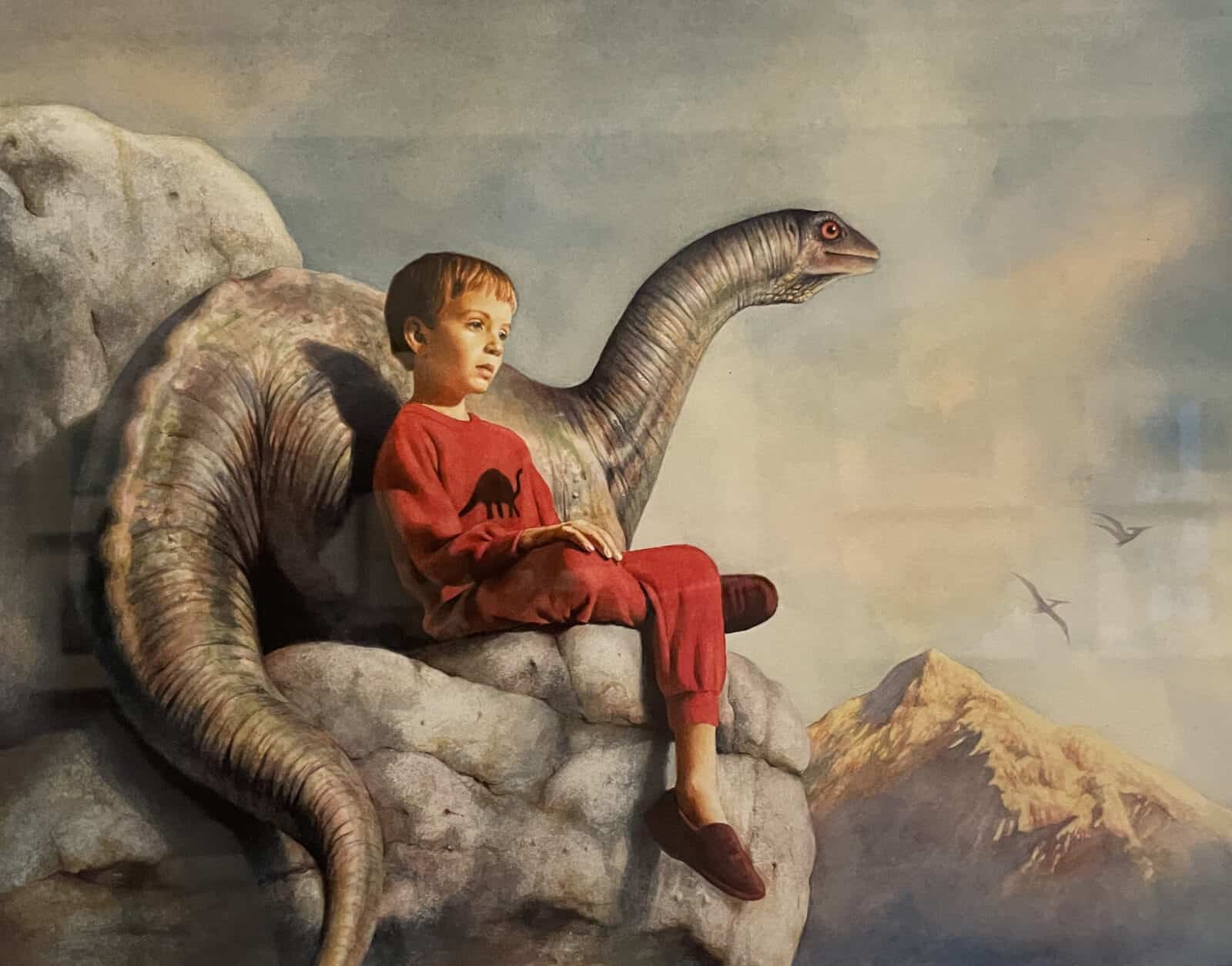 A boy and a baby apatosaurus sit together on a rock in the sun in Dennis Nolan's Dinosaur Dream. Press image courtesy of the Norman Rockwell Museum