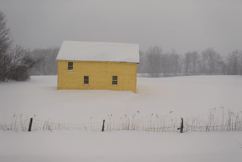 A yellow barn shows up warmly in falling snow. Press courtesy photo.