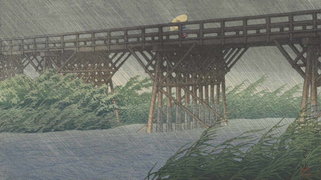 Rain falls over a river and a figure with an umbrella in Evening Shower at Imai Bridge by Hasui Kawase. Press photo courtesy of the Clark Art Institute.