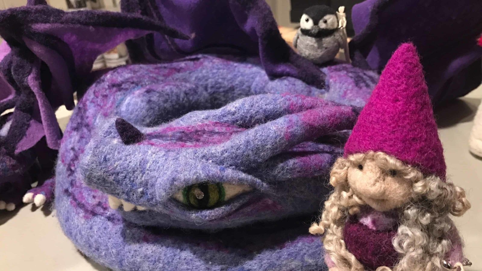 A purple dragon curles around a purple-capped girl in a Going Gnome felted wool sculpture.
