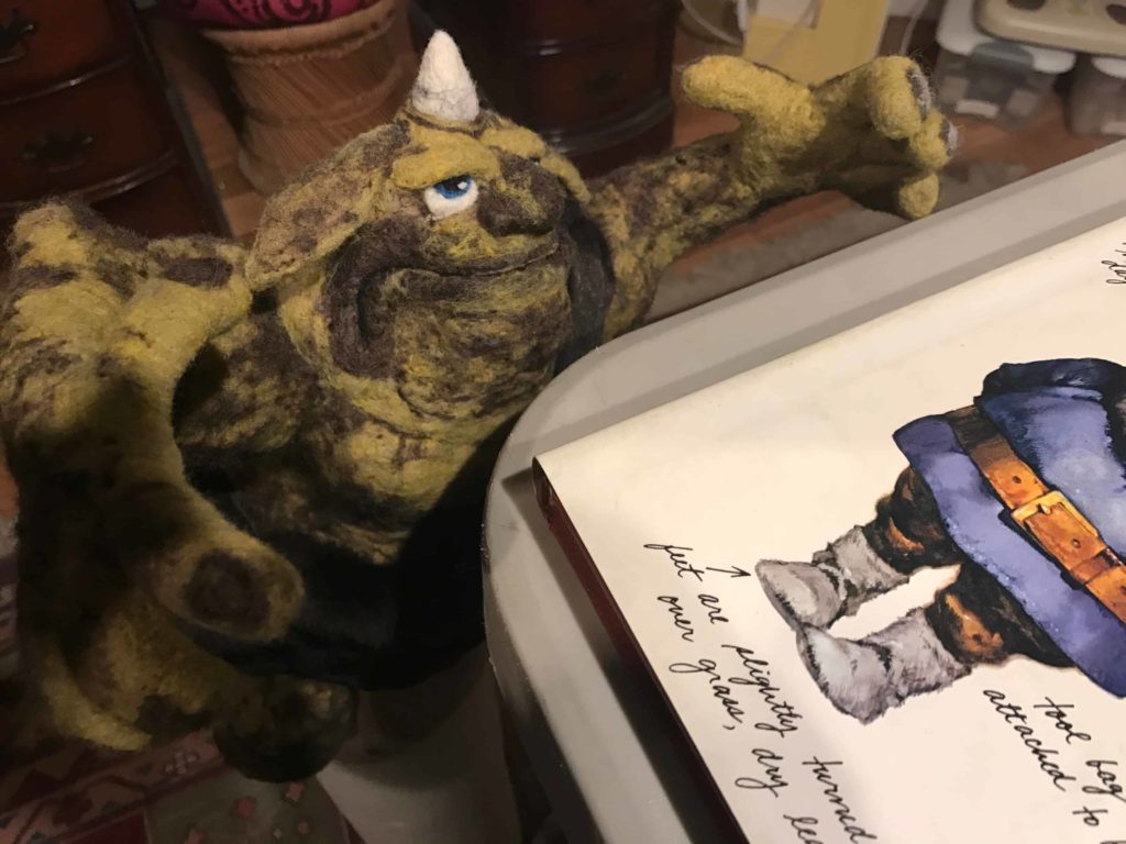 A one-horned monster reads a book of gnomes in a Going Gnome wool sculpture.