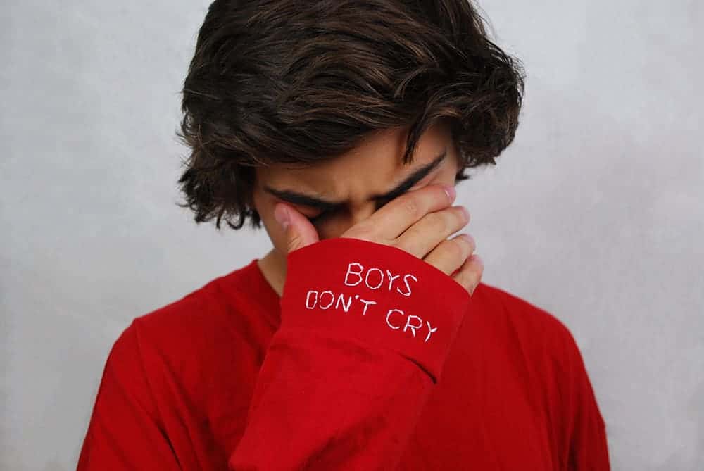 A short-haired youth with a hand over their eyes wears a red shirt with 'Boys Don't Cry' on one cuff, in the Spectrum exhibit at MCLA's Gallery 51 in North Adams.
