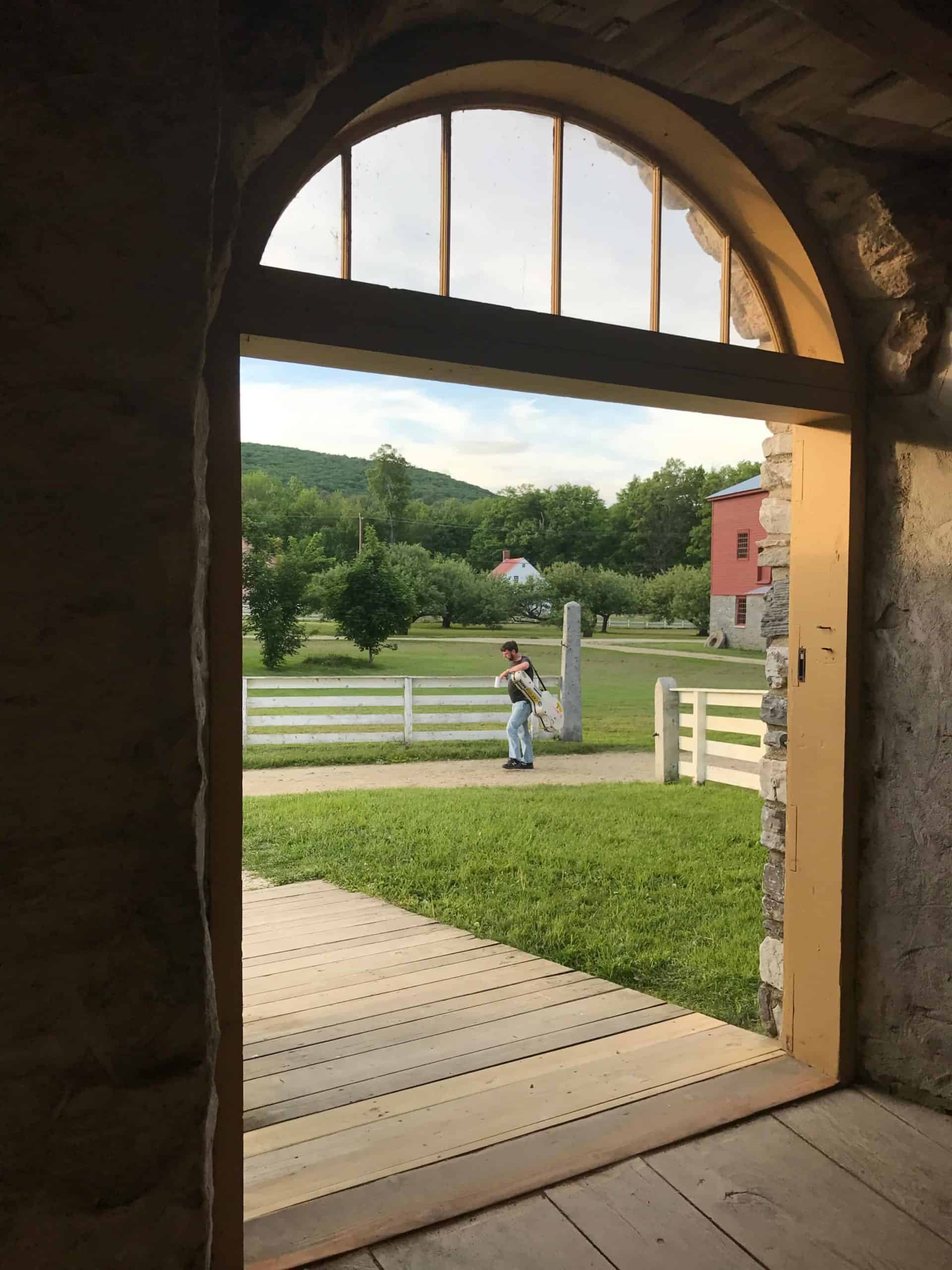 A musician walks by the round stone barn.