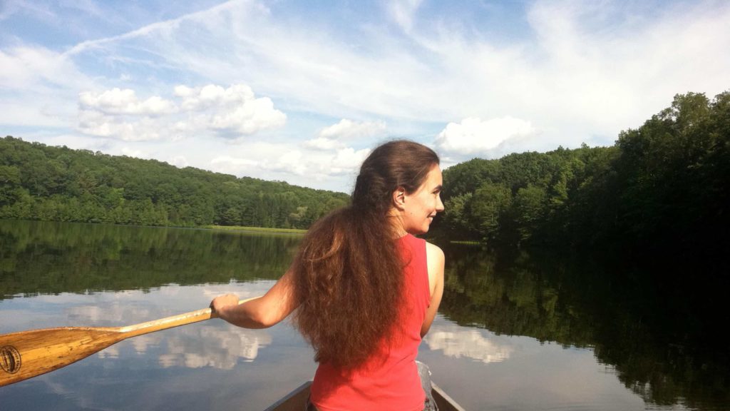 Kate Abbott paddles a canoe on a quiet pond.