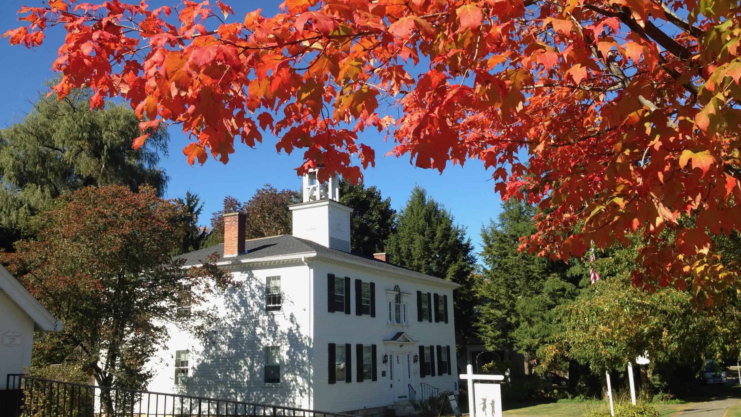 A sugar maple shows color near the historic Lenox Academy Building on a sunny fall day.