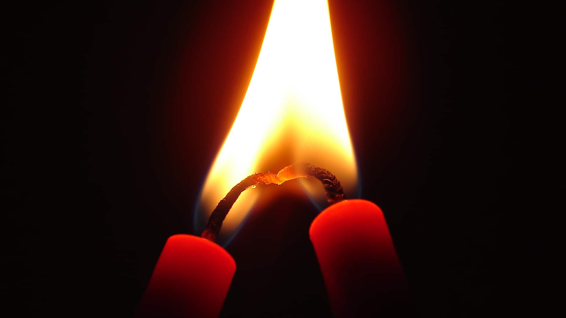 Candle flames meet in the dark. Photo by Nevit Dilmen