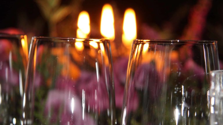 Wine glasses glint in candle light.