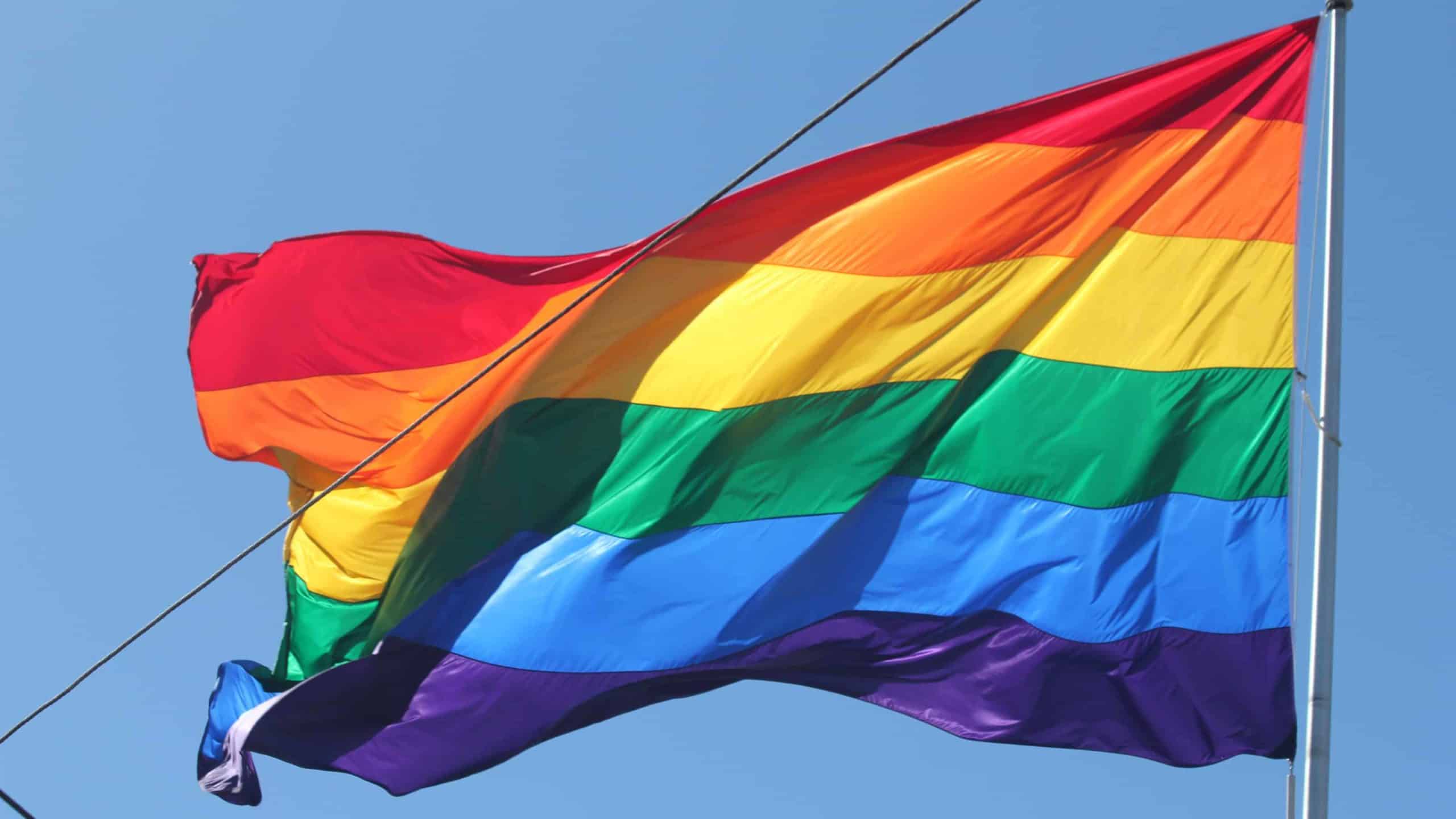 An LGBTQA Pride flag flies in a clear blue sky.