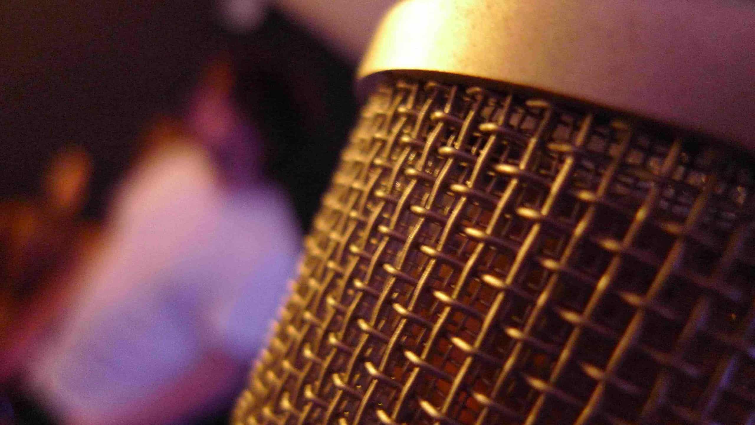 A microphone shimmers close-up in purple and gold lighting. Creative Commons courtesy photo.