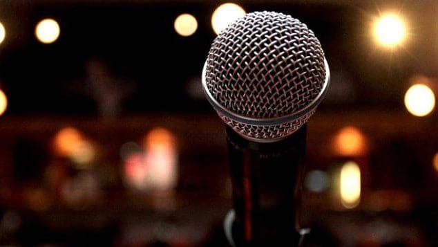 A microphone gleams in the dark with points of light in the background. Creative Commons courtesy photo.