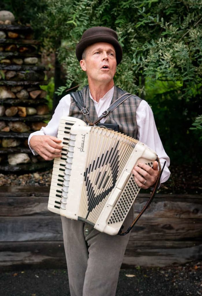 A musician walks through the twilight singing and playing accordion in Double Edge Theatre's 'We the People.'