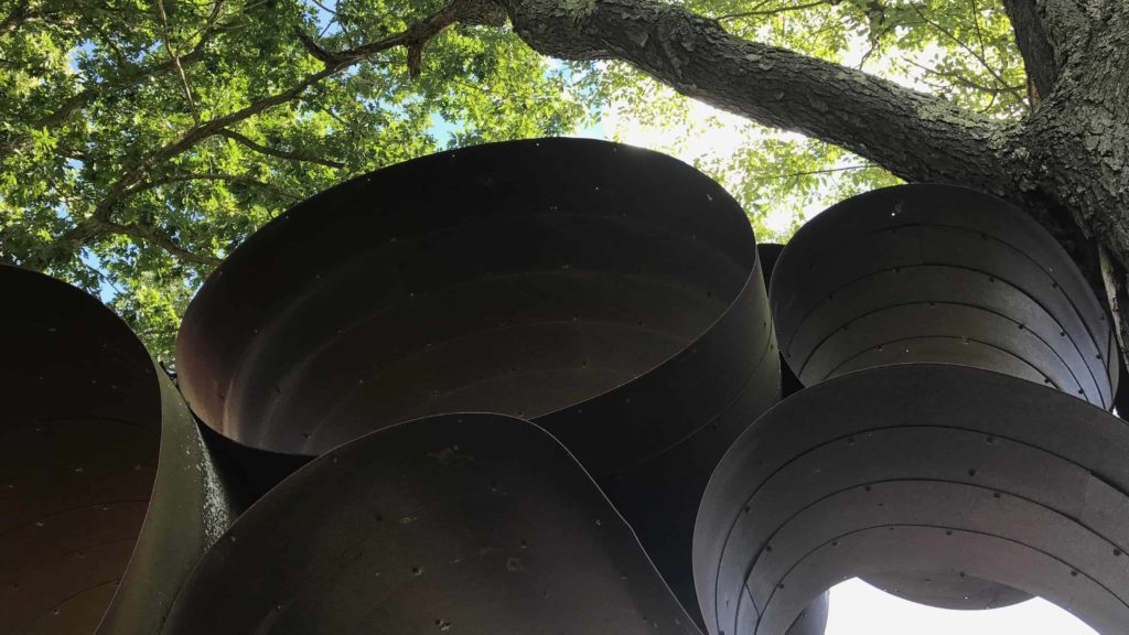 Hoops of metal ripple between maple trees in the sculpture park at Art OMI.