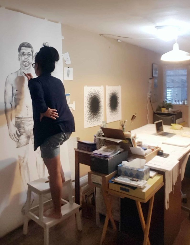 Artist Trinh Mai works on a life-sized portrait of ehr husband, Hien, as she creates an art installation in her studio in Southern California. Image courtesy of the artist.