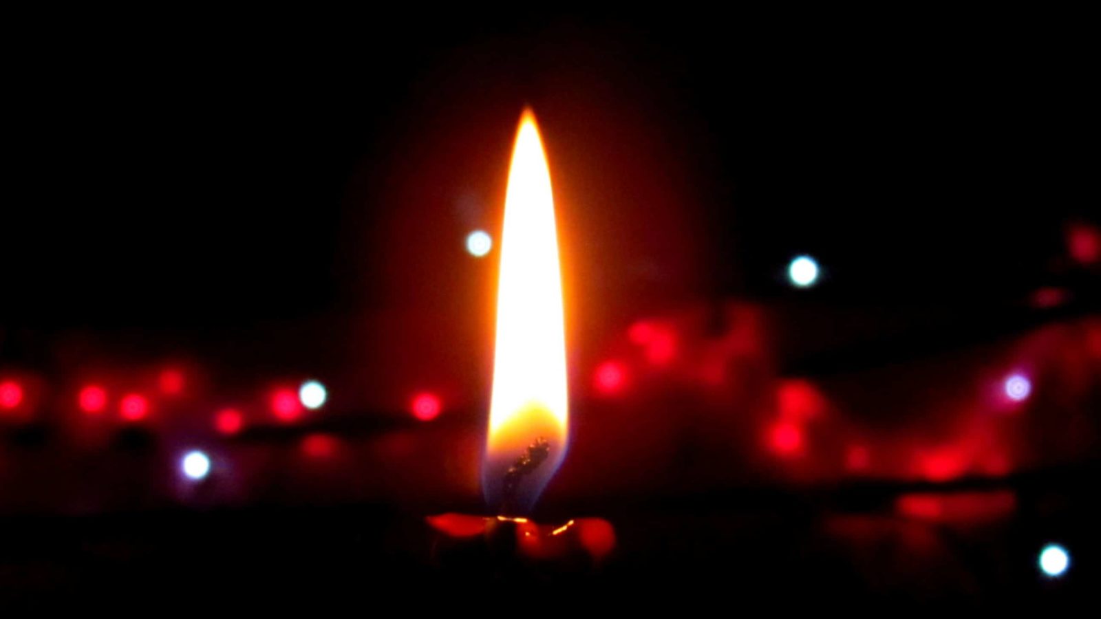 A candle burns in a dark room, touching off gleams of red.