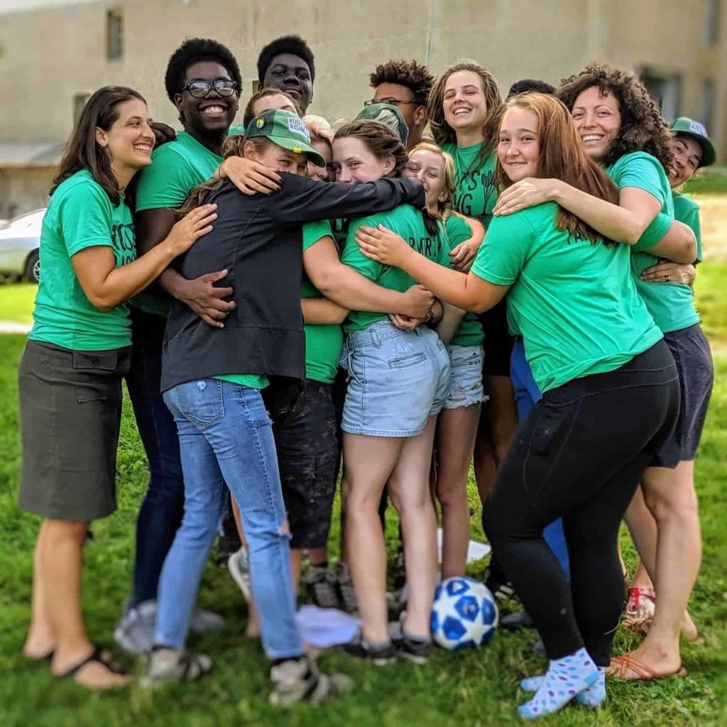 Teen members of the Roots Rising farm crew lean into a group hug.