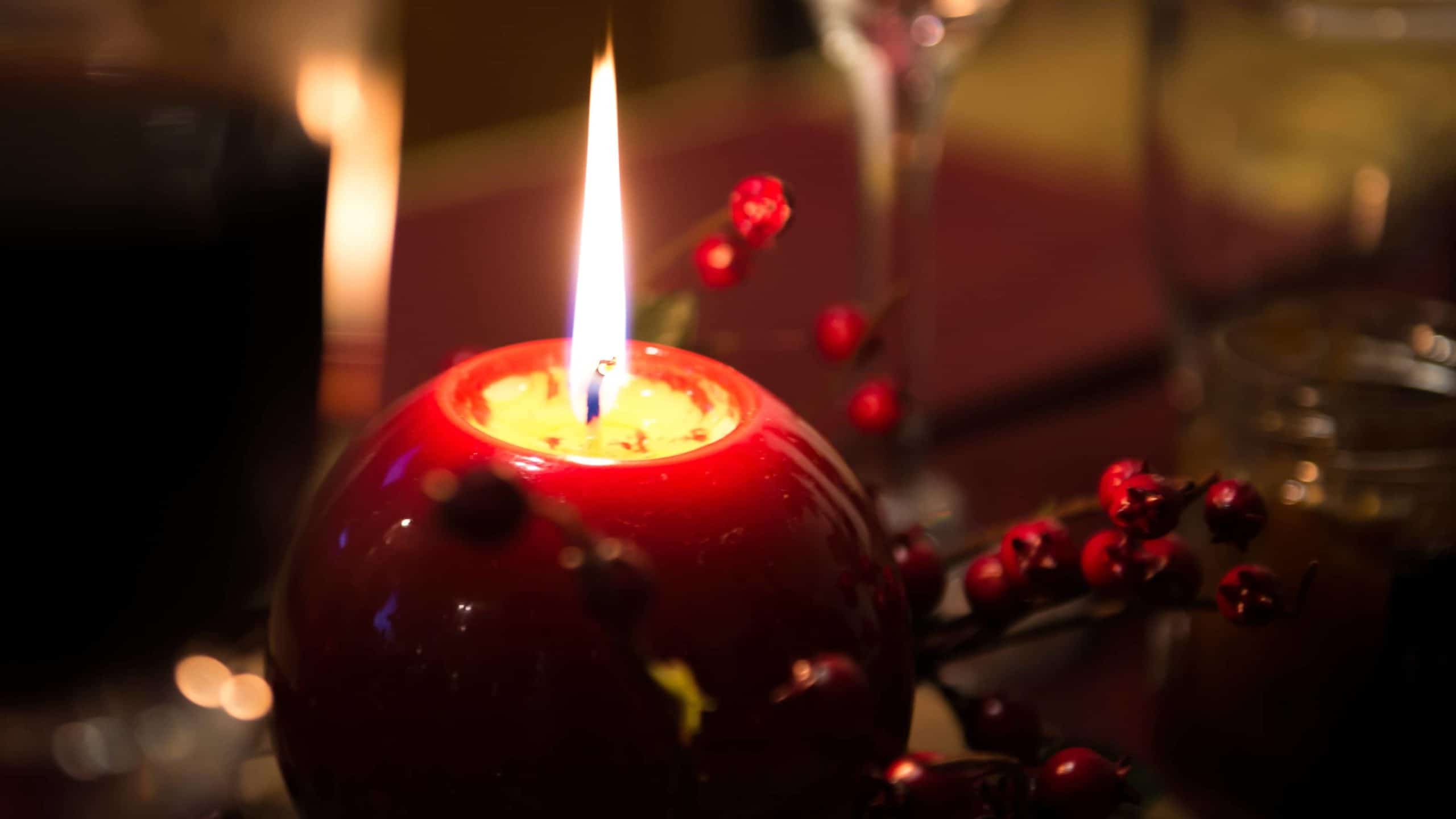 A holiday candle burns in a red globe beside winterberry.