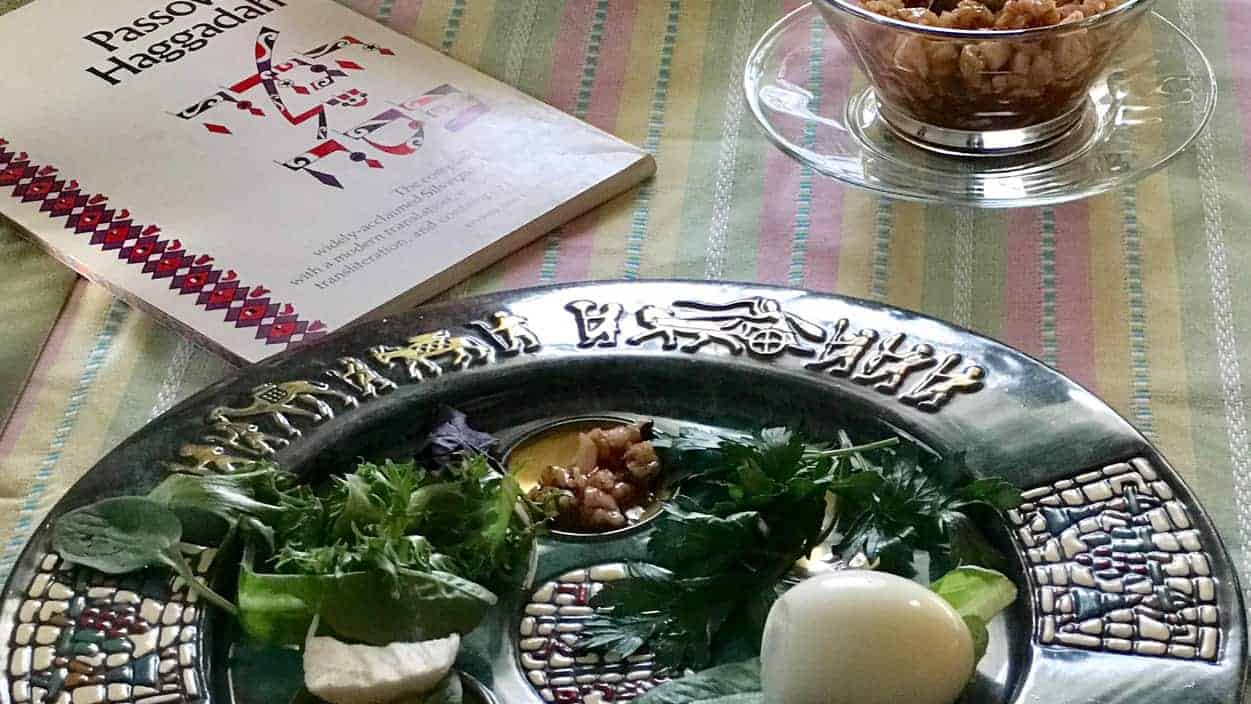 A Seder plate sits by a glass bowl of charoset and a Haggadah for Pesach (Passover).