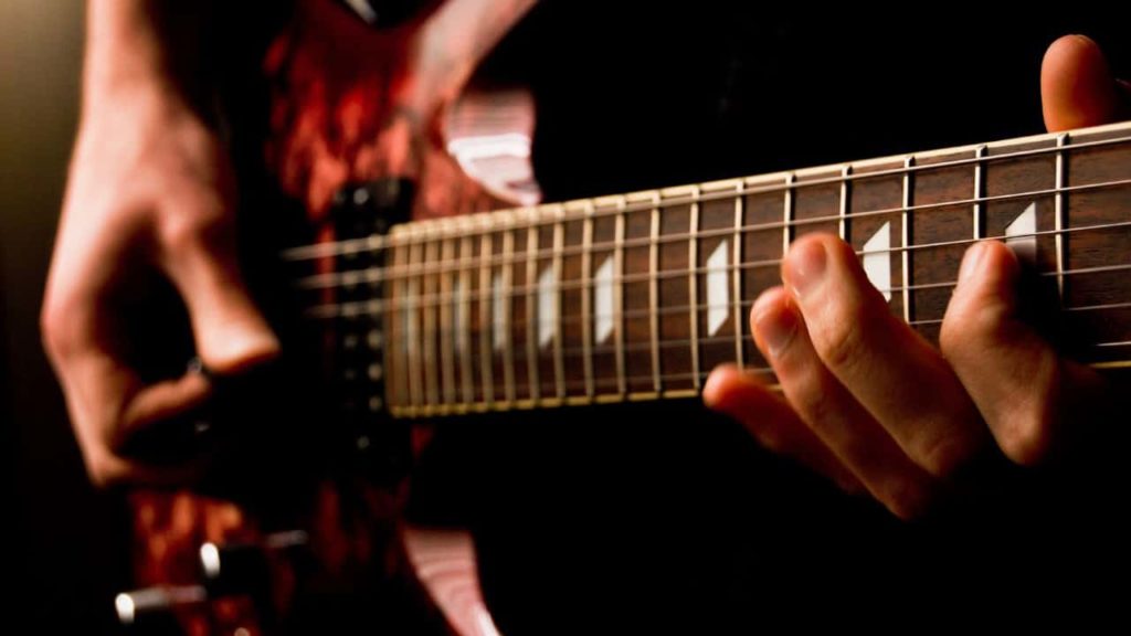 Fingers form chords on a bass guitar with a sounding board mottled like mahogany.