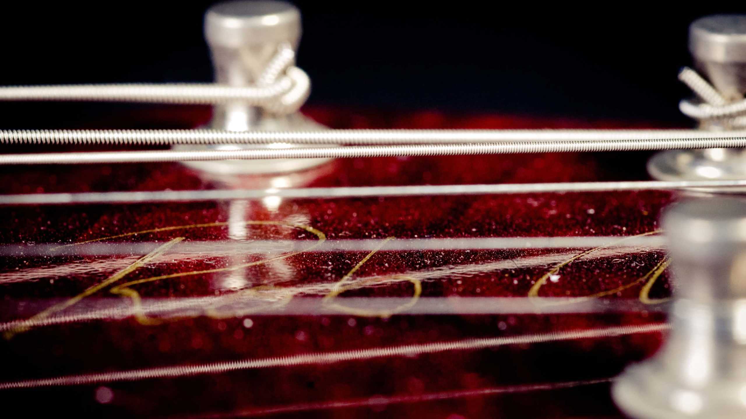 Close up, the strings and pegs of an electric guitar gleam silver in the dark.
