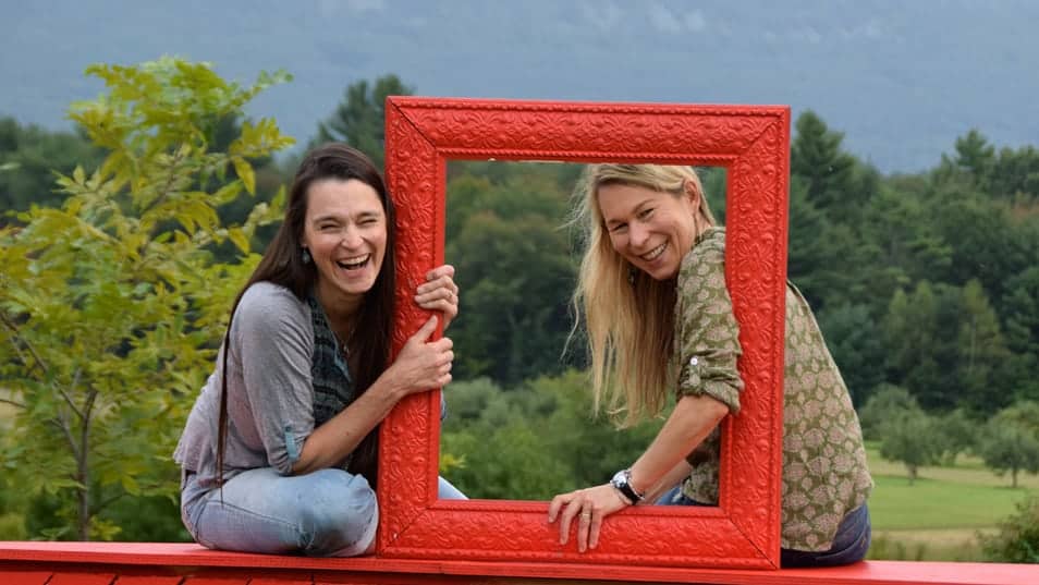 Singer songwriters Narissa and Katryna Nields laugh as they look through a sculptural metal frame in the mountains. Press photo courtesy of the artists.