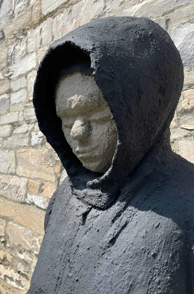 Matthew Perry's sculpture Waiting (for Trayvon Martin), a young man in a hoodie, stands with his eyes closed in the courtyard at Bennington Museum.