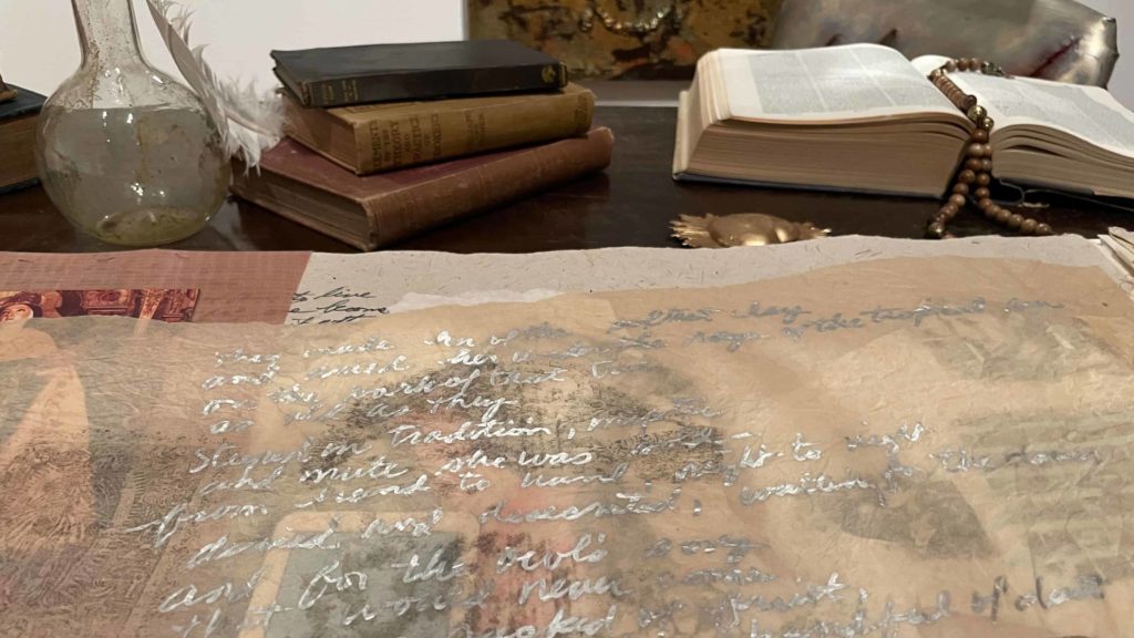 Long scrolls of paper unroll on a desktop in a closeup from Amalia Mesa-Bains' installation, The Library of Sor Juana Inez de la Cruz at WCMA