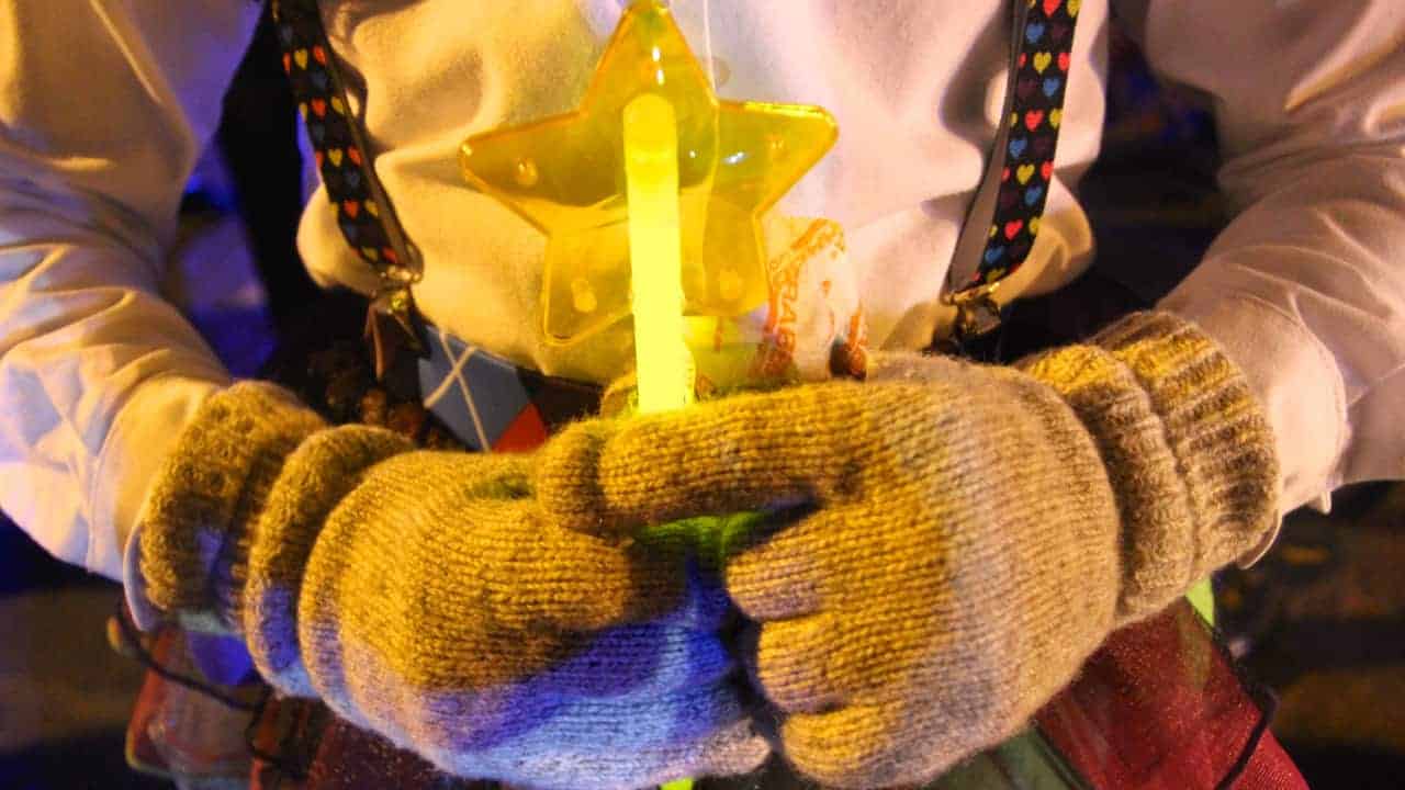 A Halloween trick-or-treater holds a glow stick in gloved hands.