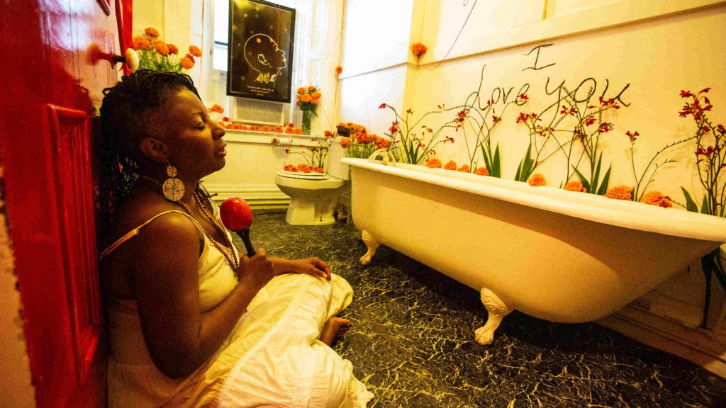 Azaria Ulmer, cure-ator and performer of Forgiveness, sits surrounded by deep orange marigolds in Rites of Passage.
