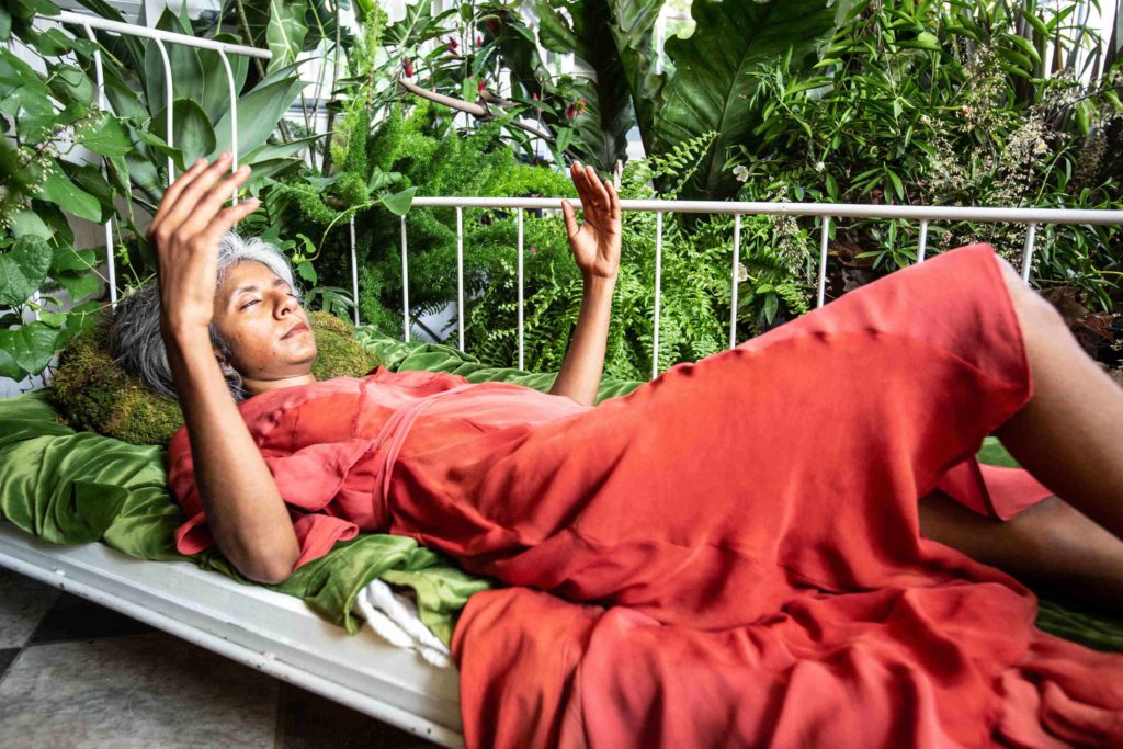Theater artist Pooja Prema lies resting among a rich array of plants in Sustenance in Rites of Passage.