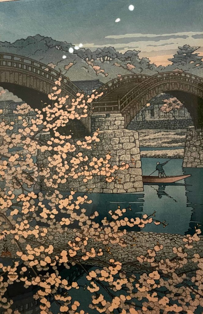 A punter skims past cherry trees in bloom in Katsushika Hokusai's Japanese wood block print of the Kintai Bridge, on display at WCMA.