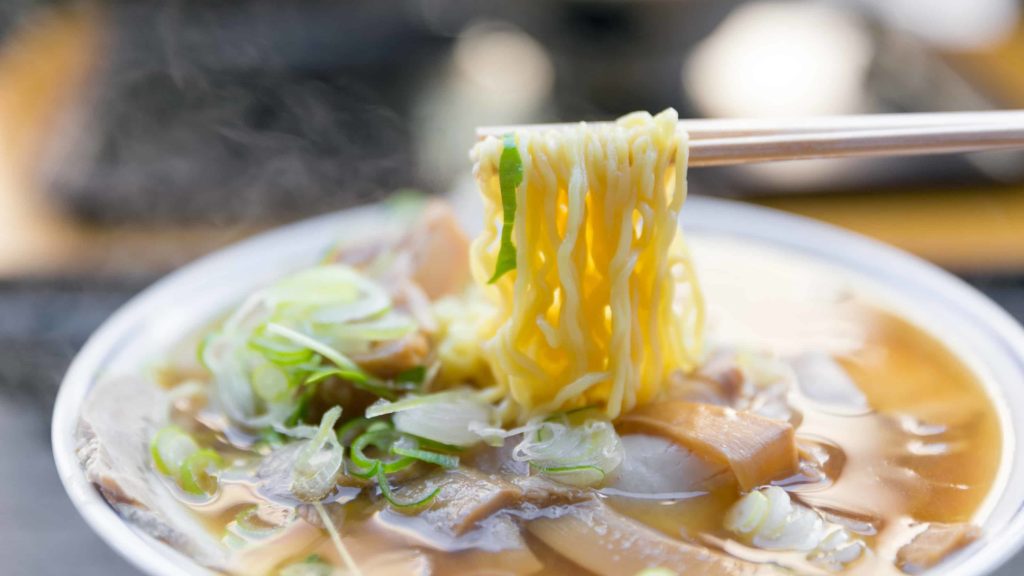 Chopsticks hold golden Ramen noodles over a bowl of broth. Creative Commons courtesy photo
