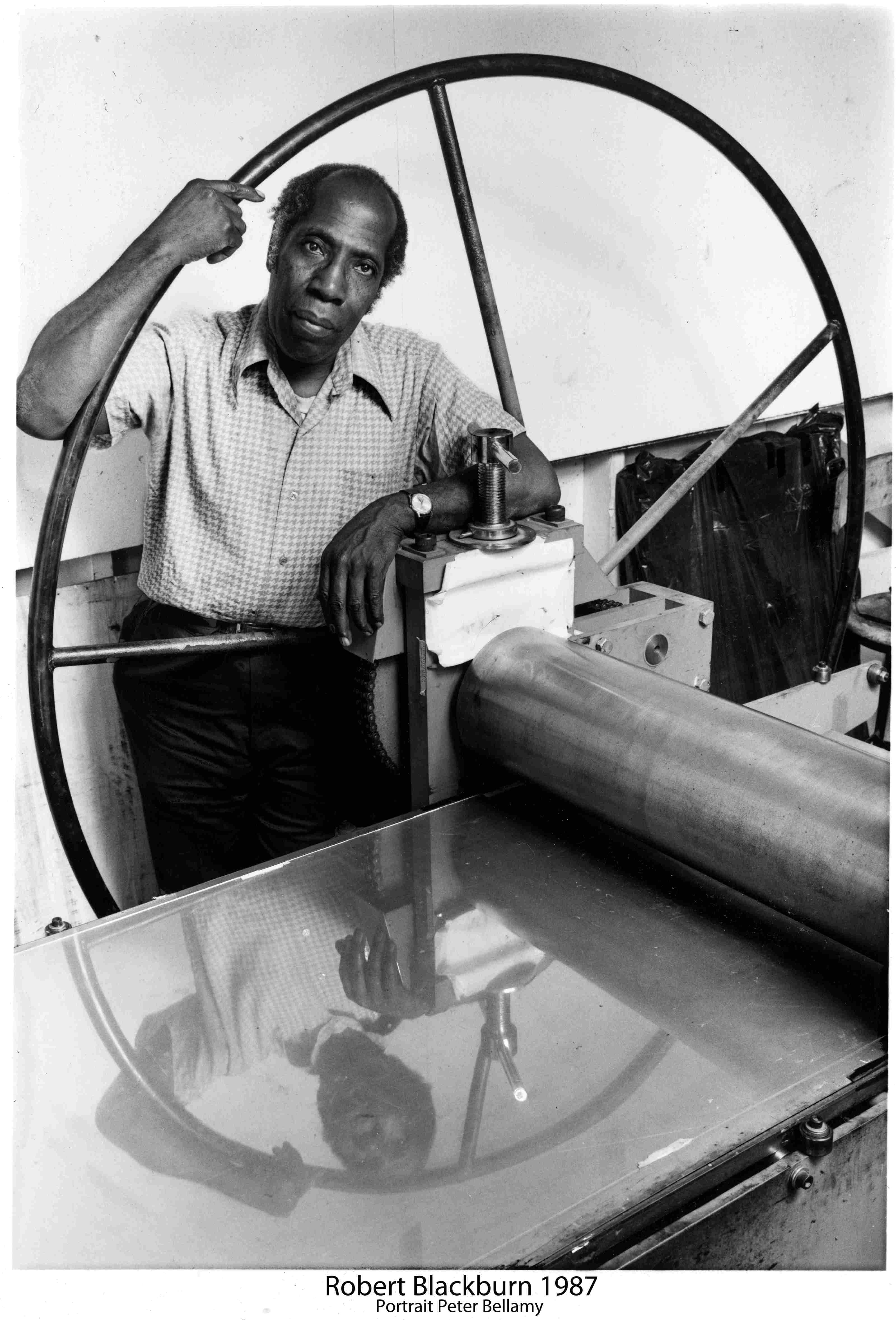 Artist and Master Printer Robert Blackburn stands by the wheel of a press in his workshop. Press image from the Smithsonian, courtesy of the Hyde Collection