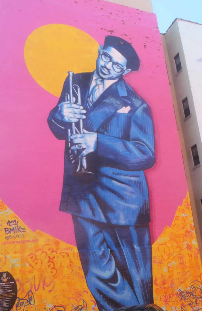 Dizzy Gillespie holds his trumpet against a vivid pink and gold swirling background in a mural by Brandan BMike Odums in Harlem, N.Y. Creative Commons courtesy photo