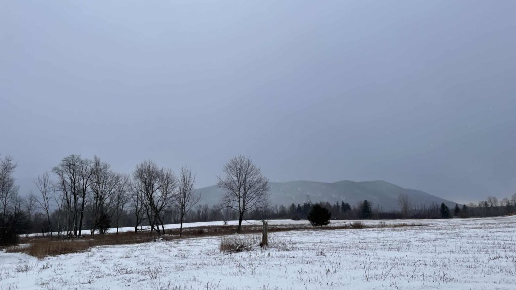 Rhe ridge shows slate blue out past snowy hayfields at Field Farm in Williamstown.