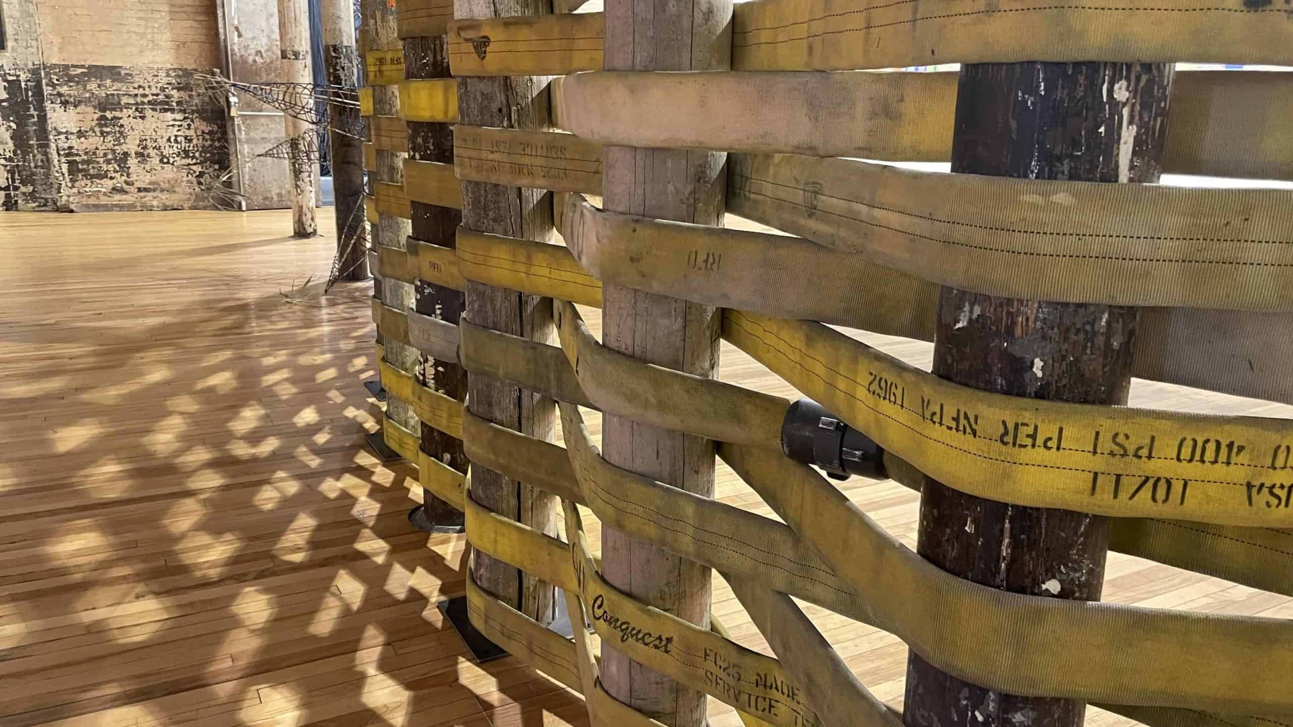 In Weep Holes at Mass MoCA, Lily Cox-Richard has woven a fire hose around pillars like a fiber around splints in a basket.