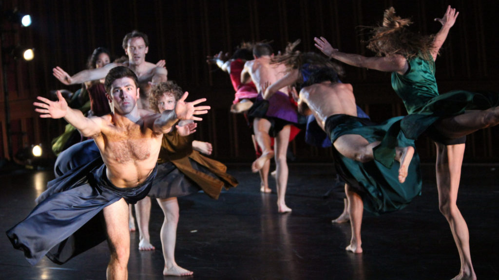 Dancers with the Mark Morris Dance Group perform, one in front holding out his arms to the camera. Press photo courtesy of the BSO