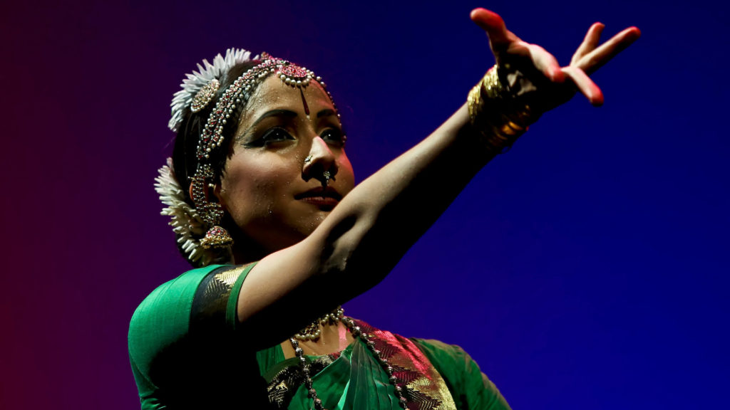 Internationally acclaimed Bharatanatyam dancer and choreographer Mythili Prakash, from Los Angeles, performs holding out a lithe arm in deep blue light.