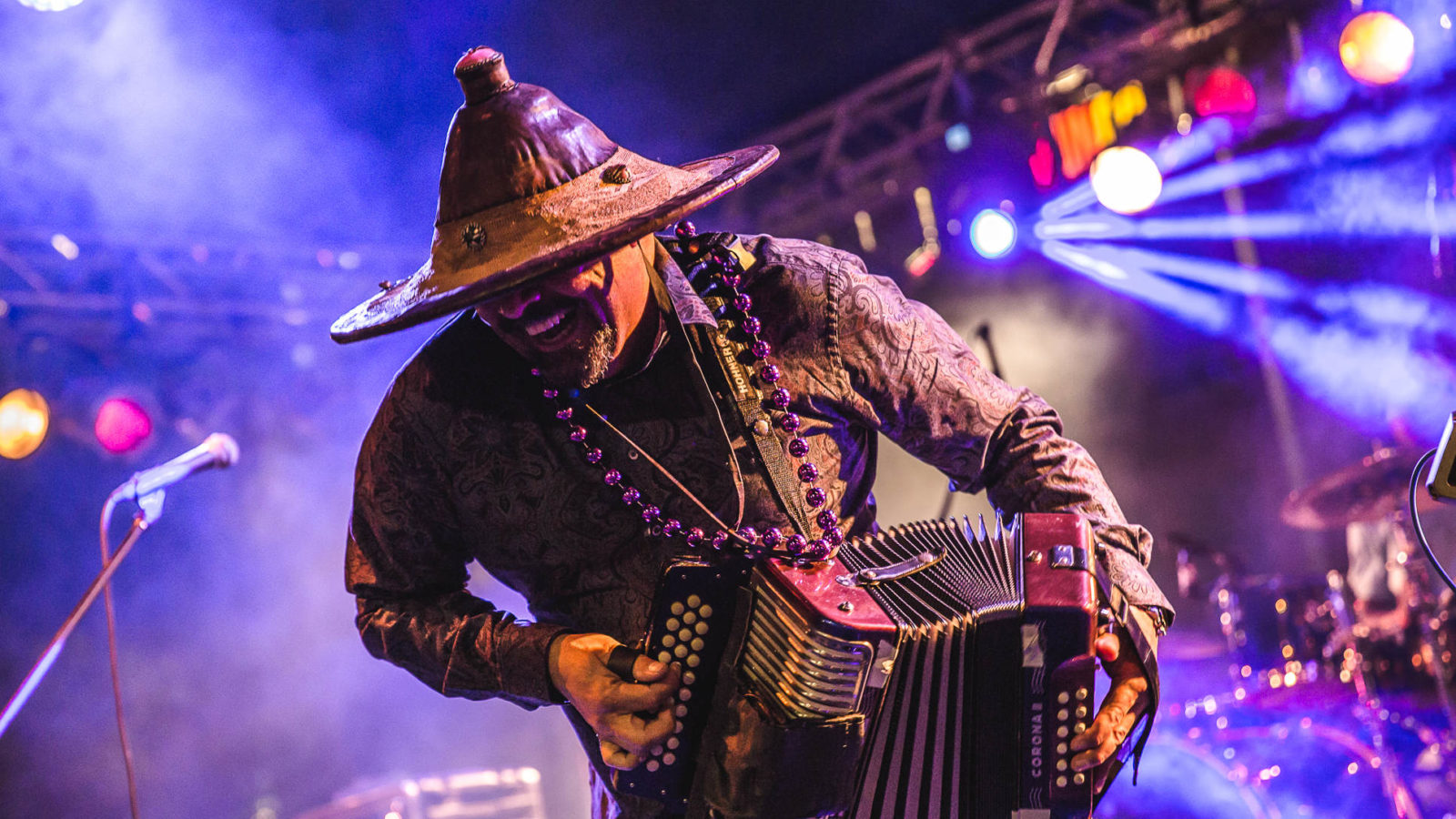 Grammy-winning Zydeco musician Terrance Ximien performs on piano accordion in his Fulani hat from Mali, laughing in purple light.