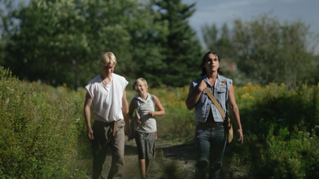 Phillip Lewitski, Avery Winters-Anthony and Joshua Odjick walk a path through a meadow in the hills in the film Wildhood. Press image courtesy of the filmmaker