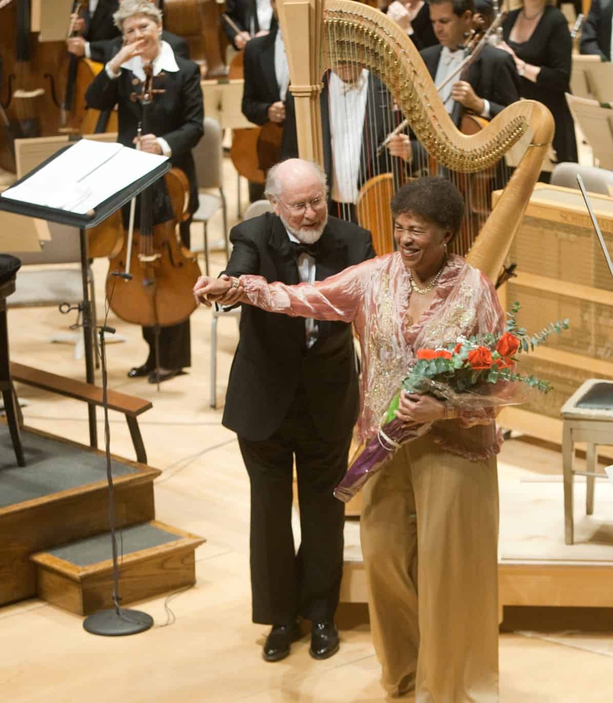 Ann Hobson Pilot holds a bouquet and stands beside John Williams with the Boston Symphony Orchestra. Press photo courtesy of the BSO