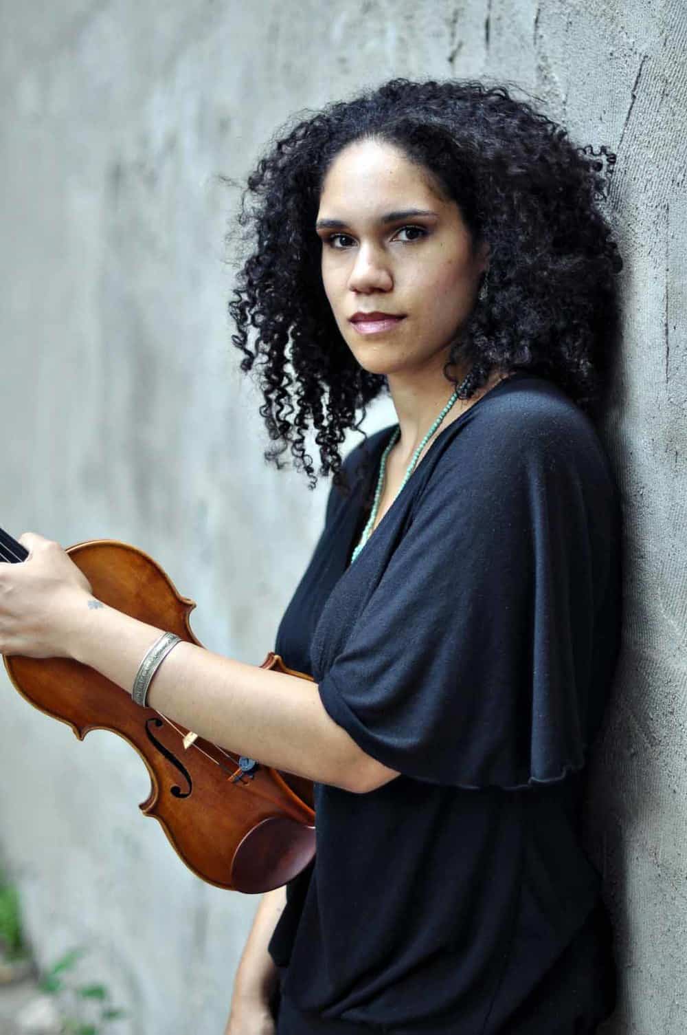 Internationally acclaimed composer and violinist Jessie Montgomery stands with her violin. Press photo courtesy of the BSO and the composer.