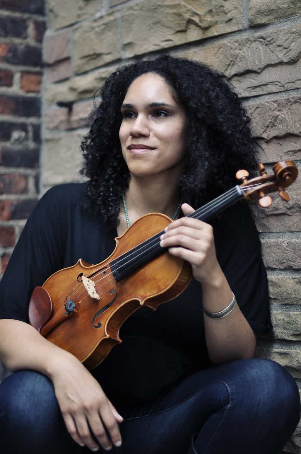 Internationally acclaimed composer and violinist Jessie Montgomery sits with her violin. Press photo courtesy of the BSO and the composer.