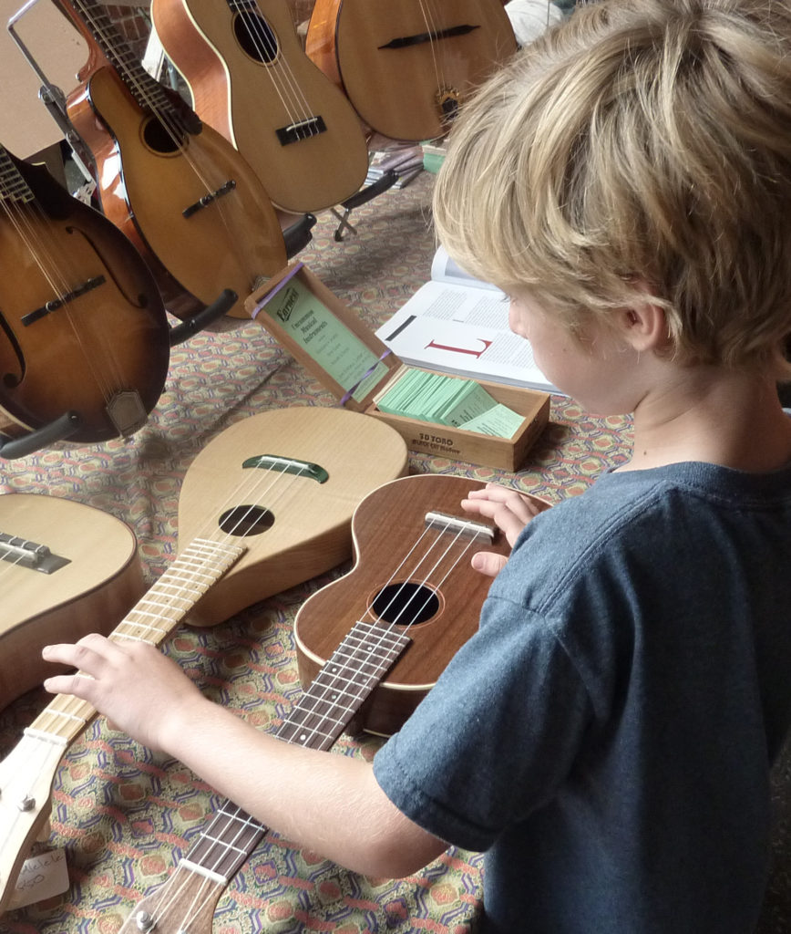 A boy looks at a table of ukuleles and mandolins at FreshGrass. Press photo courtesy of Mass MoCA