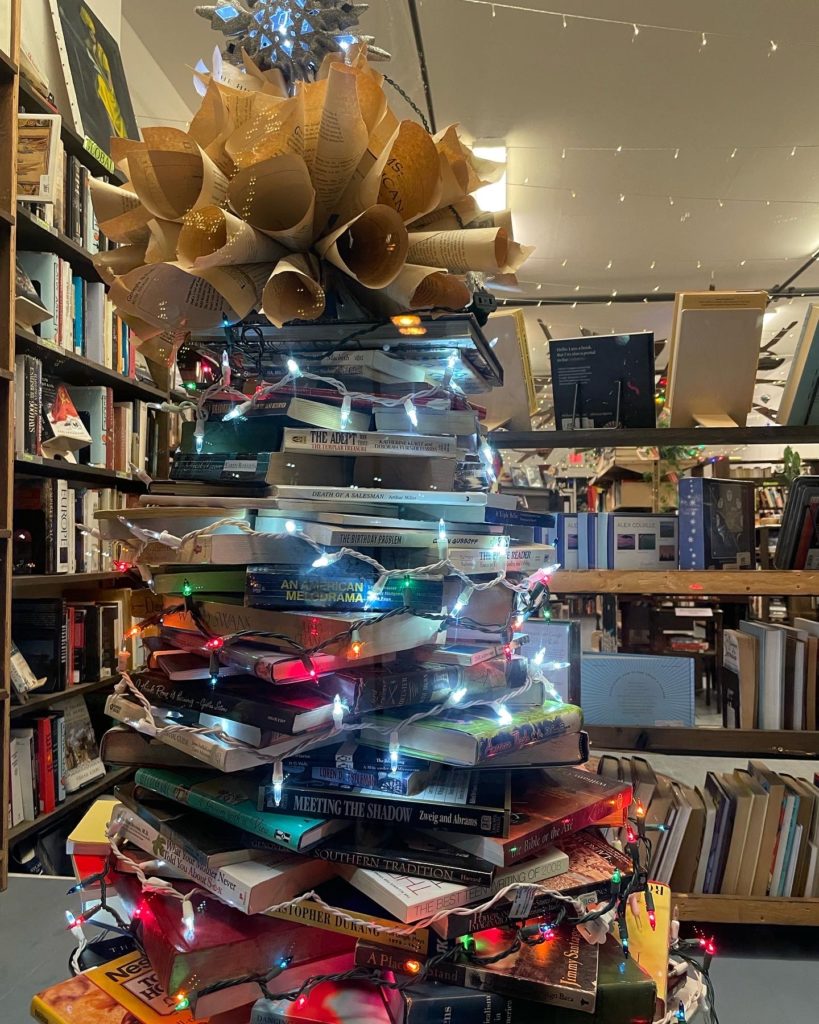 A Christmas Tree made of books glows in the window of the Bear and Bee Bookshop.
