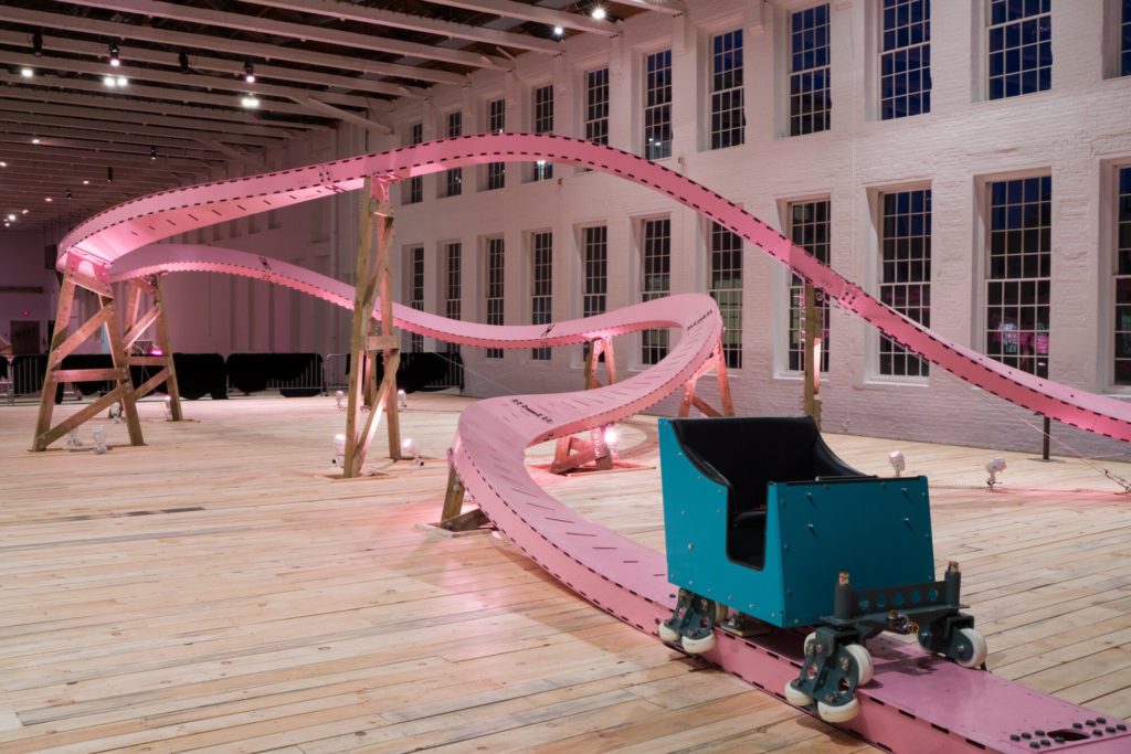 A green cart rests at the foot of the pink roller coaster track in EJ Hill's Brake Run Helix in Building 5 at Mass MoCA. Press image courtesy of Mass MoCA
