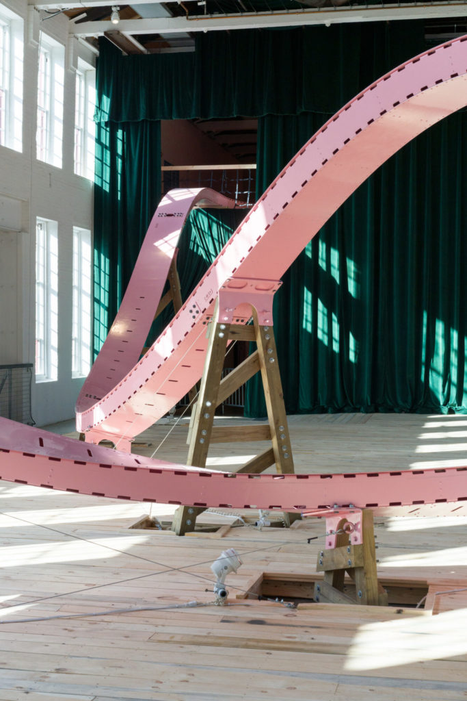 A green curtain catches sunlight behind the pink roller coaster track in EJ Hill's Brake Run Helix in Building 5 at Mass MoCA. Press image courtesy of Mass MoCA