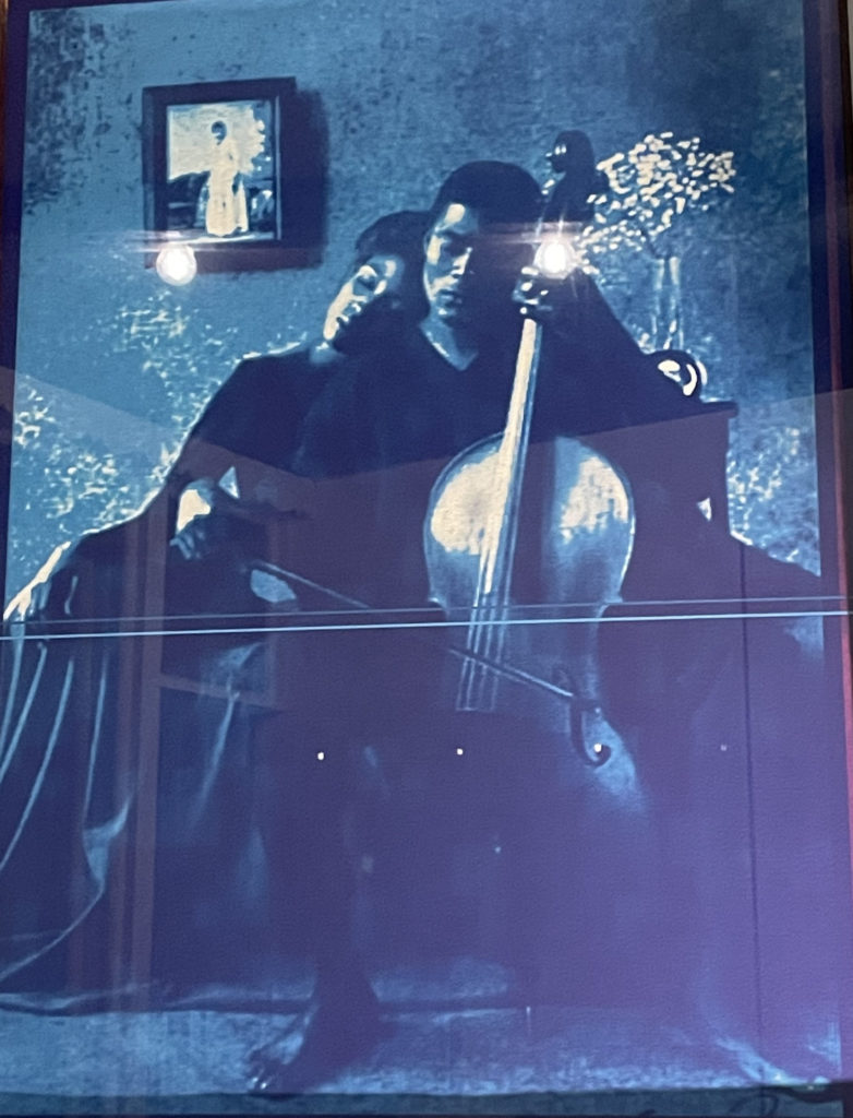 A Black man plays the cello softly as a woman leans on his shoulder at dusk, in a photograph in Lorenzo Baker's new work at MCLA. Press image courtesy of the artist