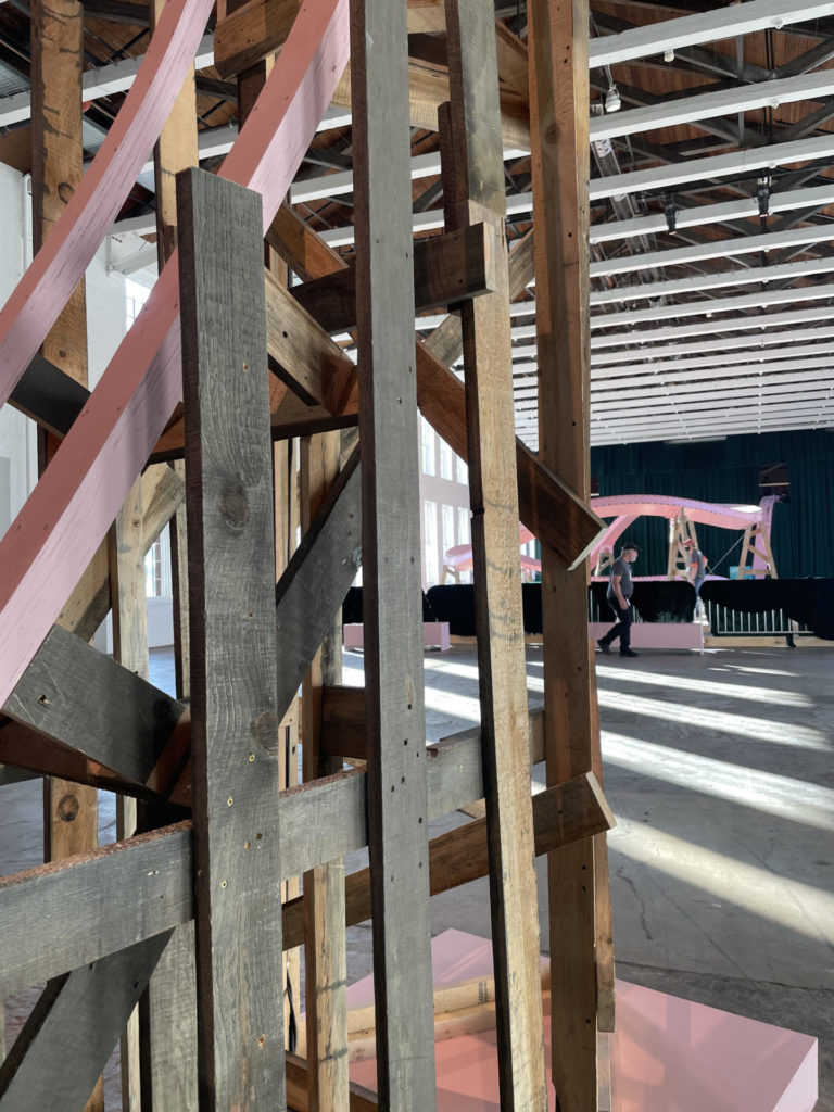 Sunlight falls through the wooden scaffold of roller coaster tracks in EJ Hill's Brake Run Helix in Building 5 at Mass MoCA.
