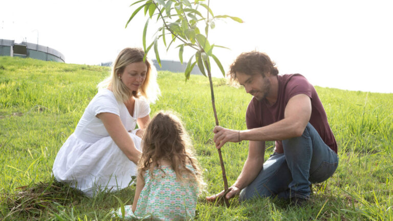 Two adults and a child plant a tree on a sunny law in 2040, award-winning director Damon Gameau's documentary.